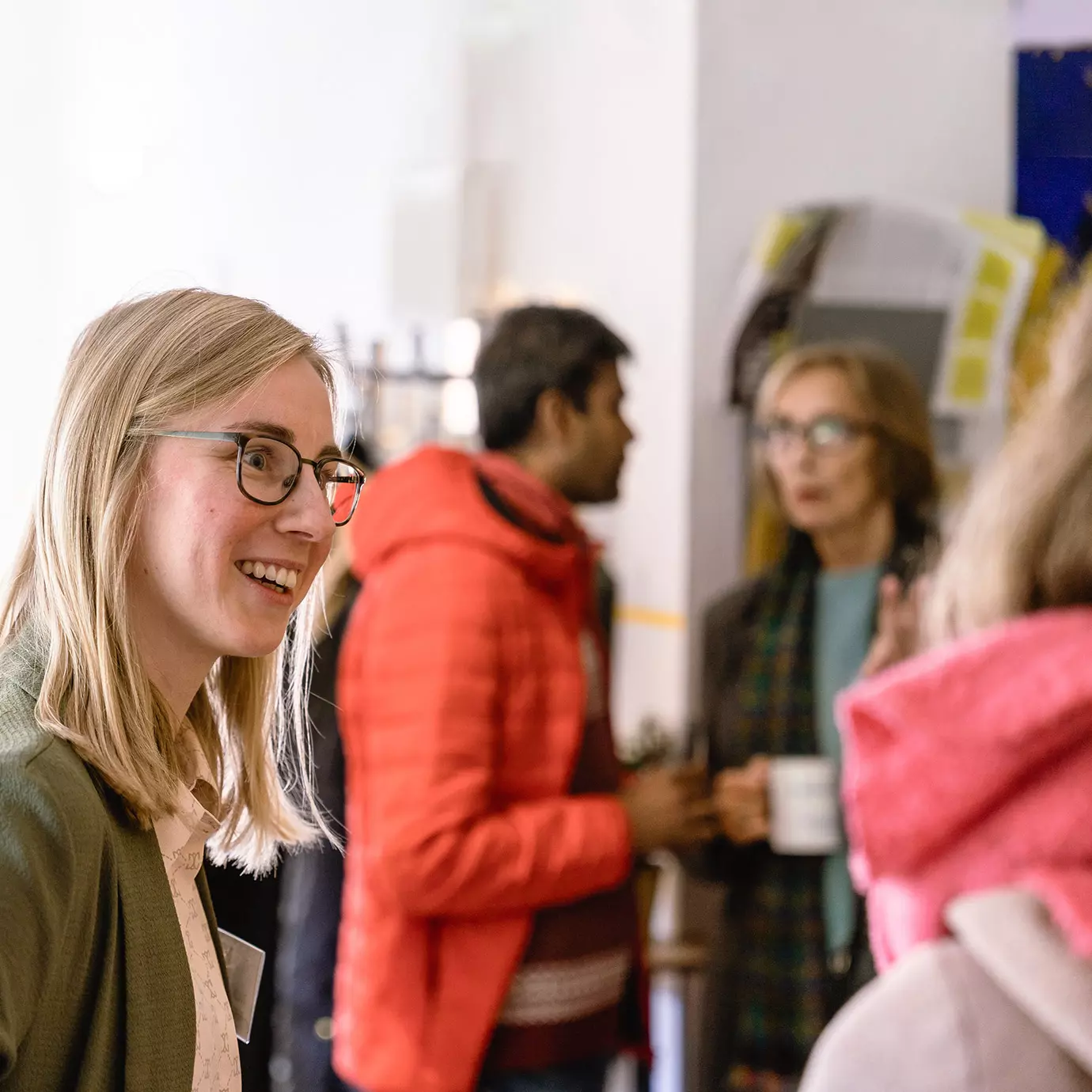 Gruppe von Menschen in Innenraum, einige stehen und unterhalten sich, eine Person hält eine Tasse